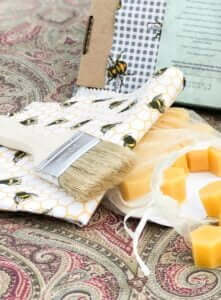 Nærbilde av en del av innholdet i settet med det du trenger for å lage bivokspapir. Blant annet vises en kost, et tøystykke av bomull og noen stykker med bivoks i en tøypose